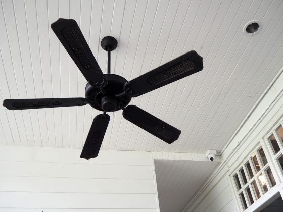 Black wood and wicker remote controlled ceiling fan mounted on thin white shiplap ceiling
