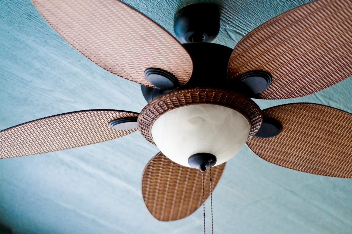 A closeup view of rustic ceiling fan blades made of wicker mounted on a blue ceiling